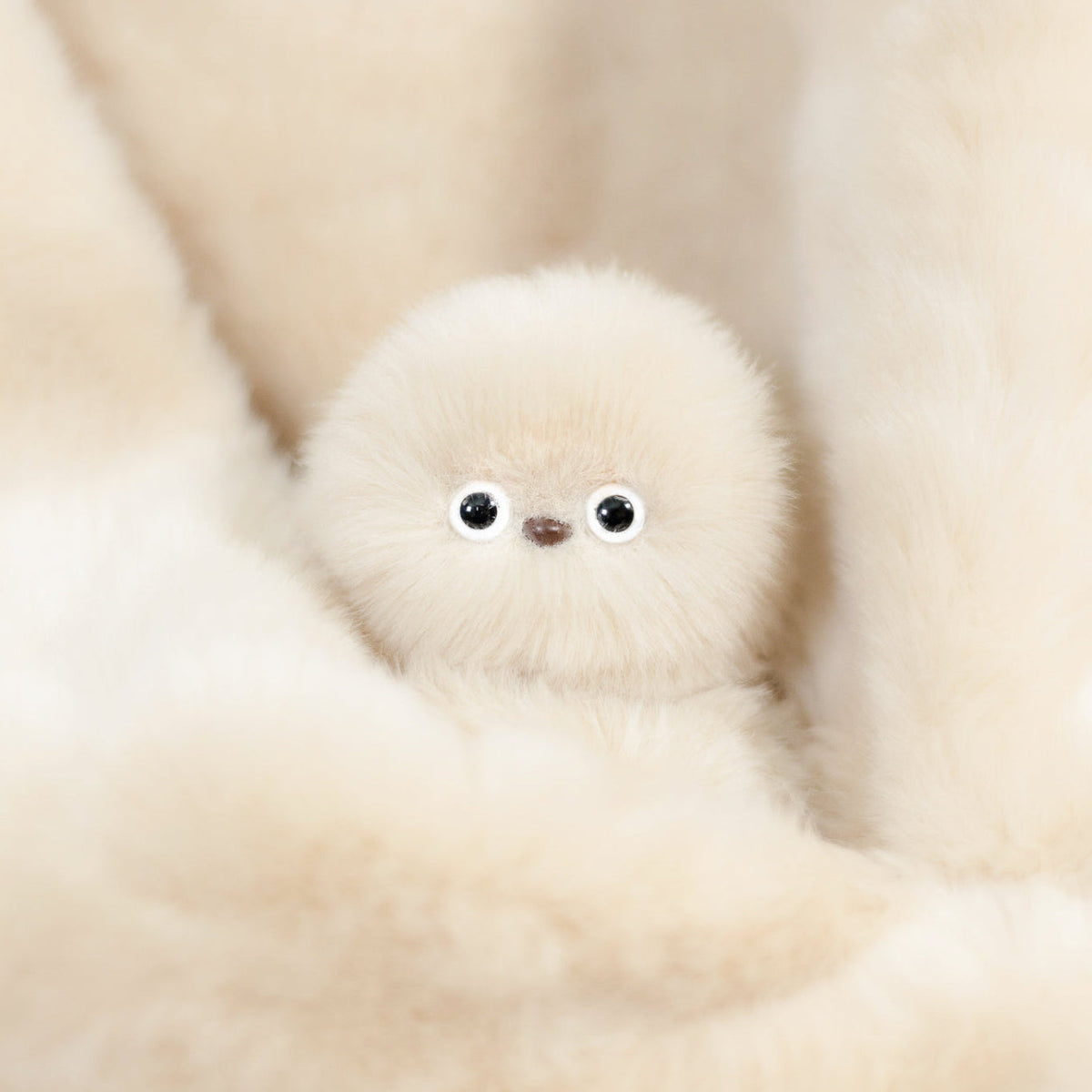 Ivory Mirumi bag charm robot resting in cream-coloured fur