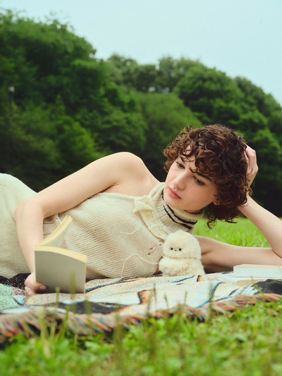 Person reading on a picnic blanket with an ivory Mirumi beside them