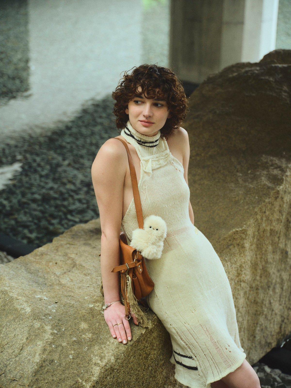Person leaning on a rock with an ivory Mirumi hanging from their shoulder bag